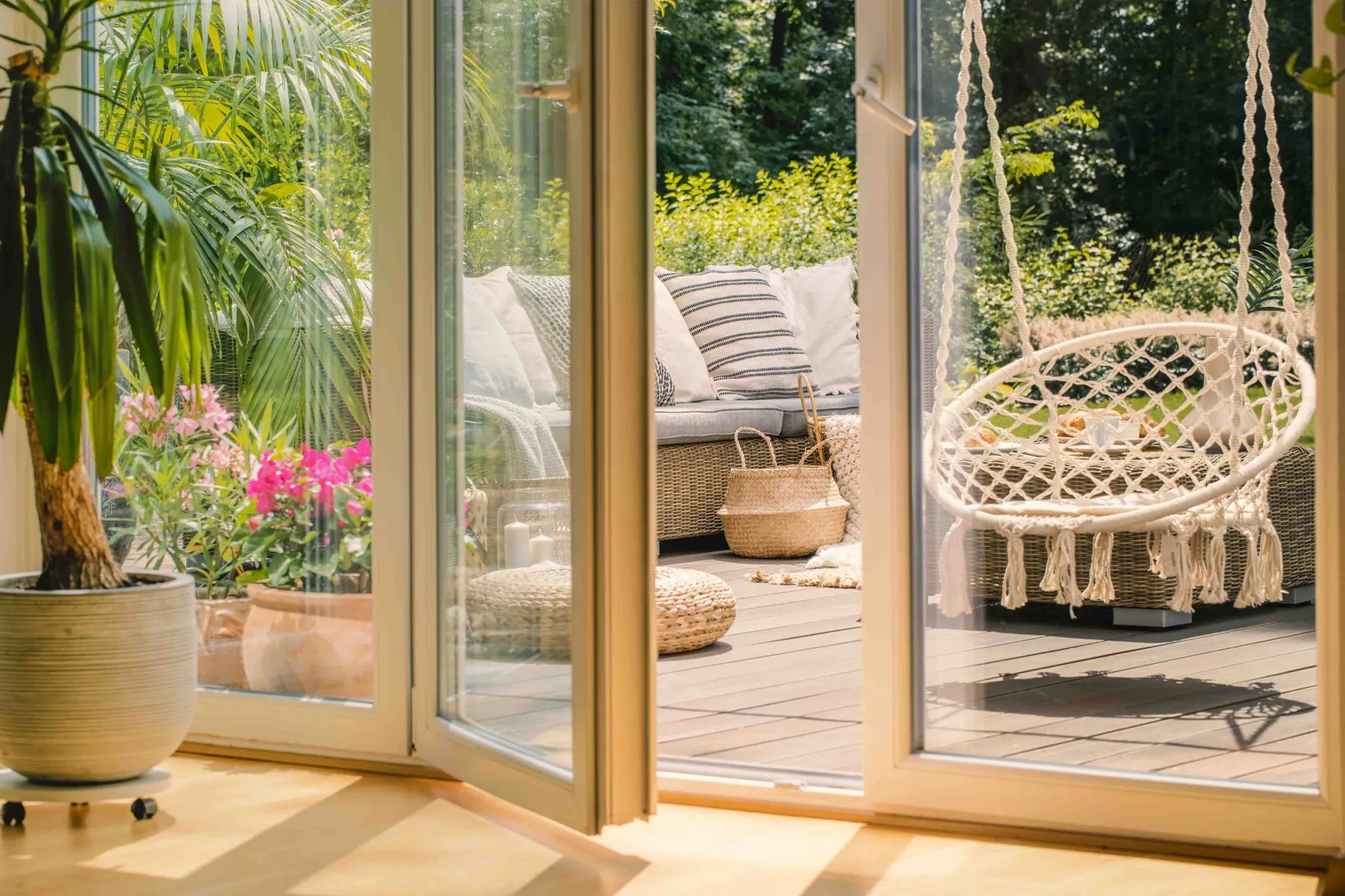 Echtes Foto eines Hängesessels und eines Rattansofas mit Kissen auf einer Holzterrasse hinter der Tür